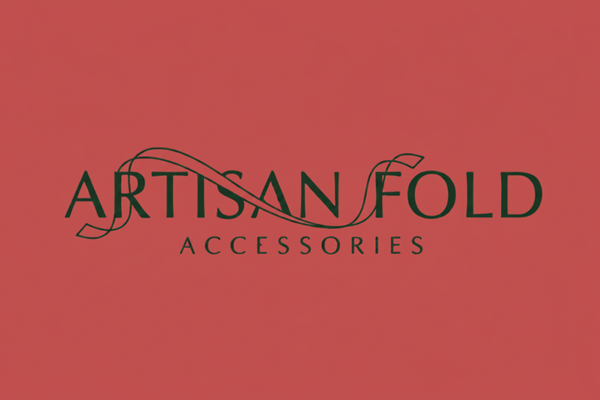 A square graphic with a coral-red background and dark gray border. Centered text reads 'ARTISAN FOLD ACCESSORIES' with a thin decorative swoosh line across the word 'ARTISAN'.